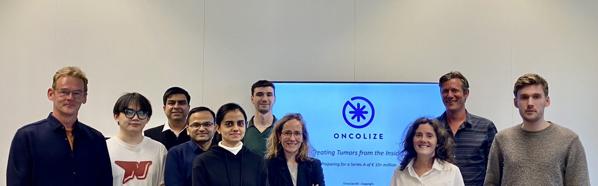Groepsfoto van een onderzoeksteam en partners in een kantooromgeving, met op de achtergrond een presentatiescherm met het bedrijfslogo van OncoLize.