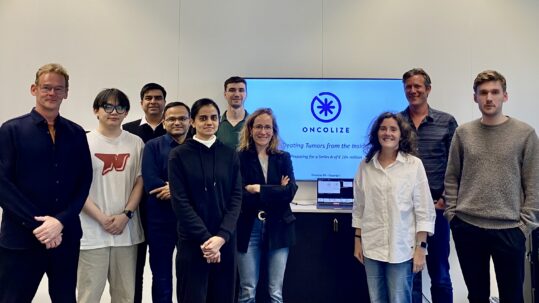 Groepsfoto van een onderzoeksteam en partners in een kantooromgeving, met op de achtergrond een presentatiescherm met het bedrijfslogo van OncoLize.