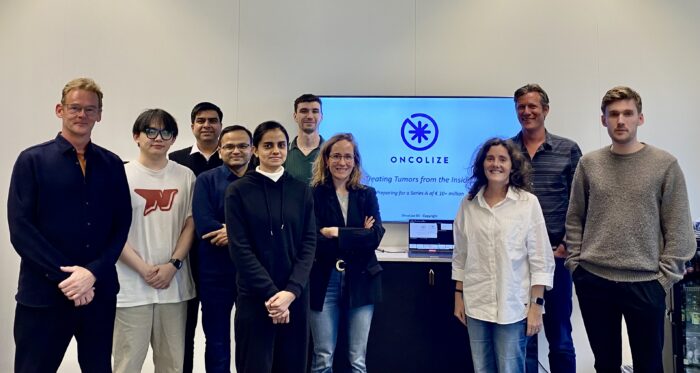 Groepsfoto van een onderzoeksteam en partners in een kantooromgeving, met op de achtergrond een presentatiescherm met het bedrijfslogo van OncoLize.
