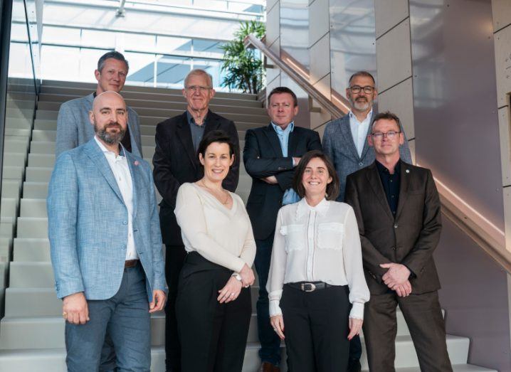 Groepsfoto van een internationale groep samenwerkingspartners in een modern gebouw, opgesteld op een trap.