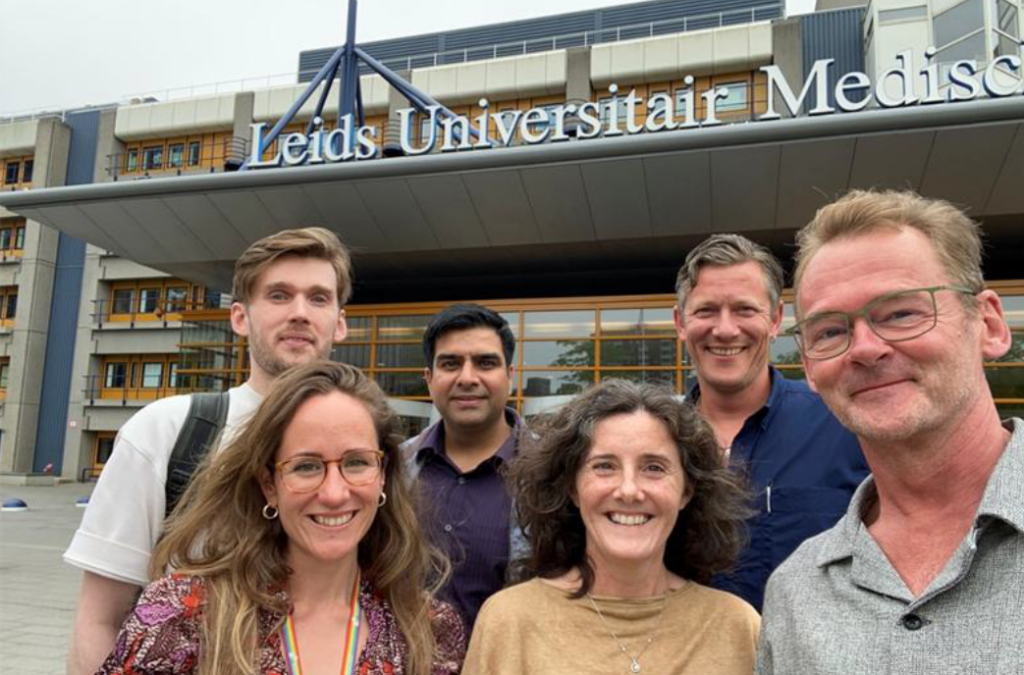 Groep mensen voor de ingang van een universitair medisch centrum, met het gebouw zichtbaar op de achtergrond.